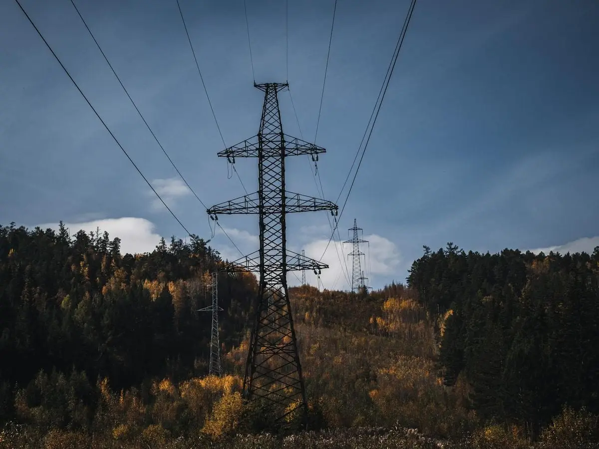 A picturesque autumn scene with transmission towers and colorful forest backdrop.