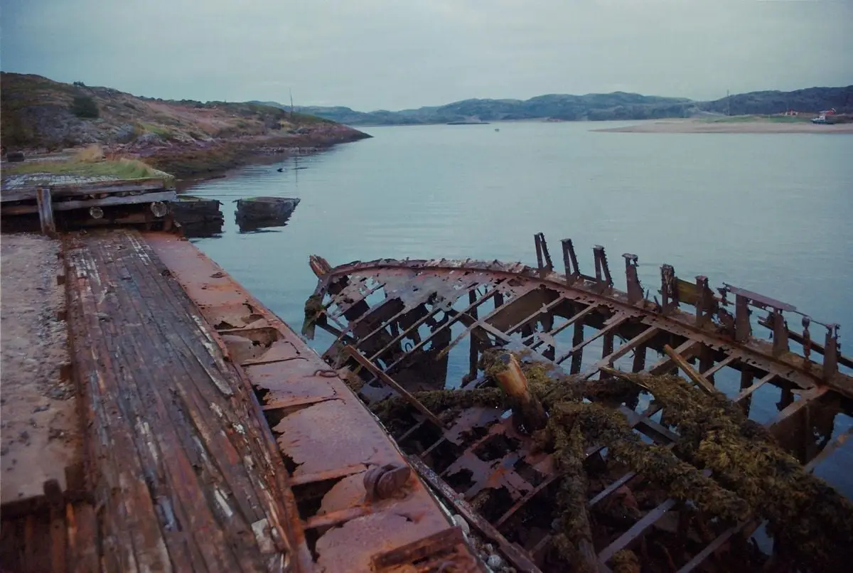 Dramatic shot of an abandoned shipwreck on a calm lake in Териберка, Russia, capturing nature's reclamation.