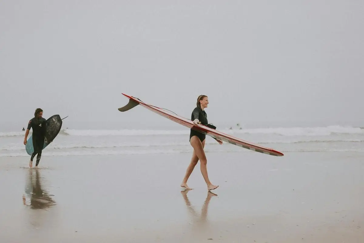 A woman carrying a surfboard on the sandy shore of Ocean City, NJ.