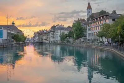 Beautiful sunset view of Thun with cityscape reflections on the river and a Ferris wheel.