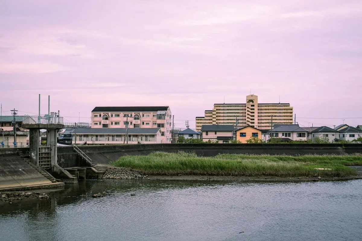 A tranquil view of Toyokawa's riverside with residential buildings under a soft pink sky.
