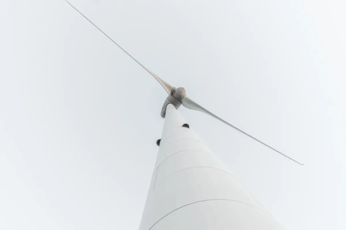 Close-up of a tall wind turbine viewed from below against a minimalistic sky.