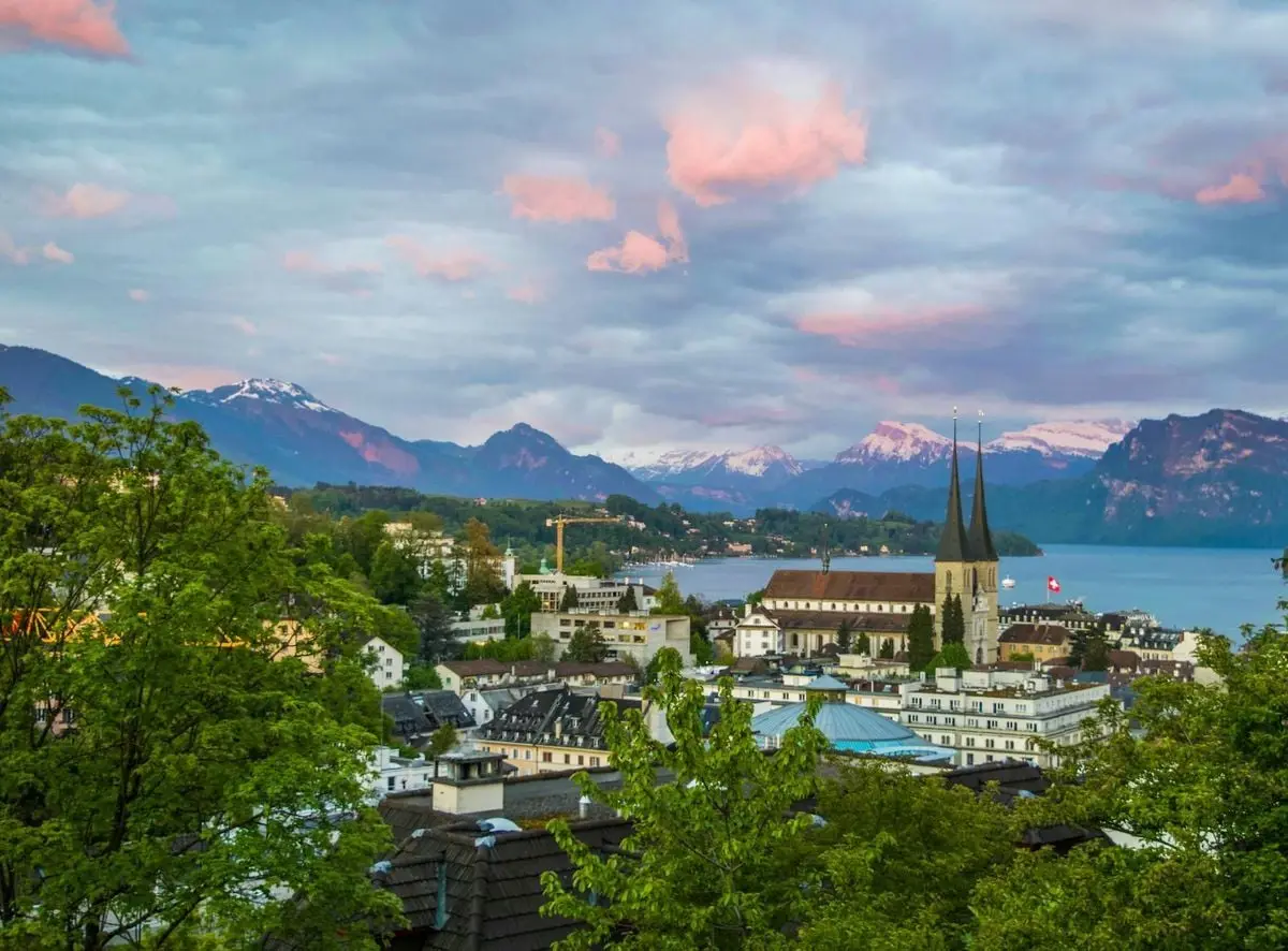 Panoramic view of Lucerne with mountains and lake at twilight, showcasing architecture and natural beauty.