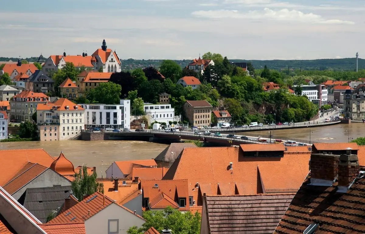 Aerial view of a picturesque European town with red roofs and lush greenery beside a calm river.