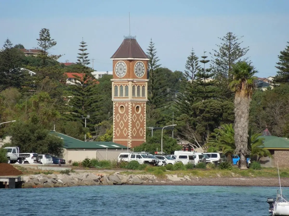 Scenic view of a vintage clock tower surrounded by trees near a waterfront setting.