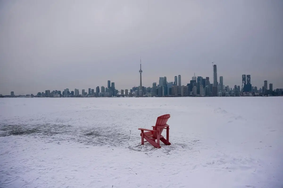 A solitary red chair overlooks the snow-covered landscape and the iconic Toronto skyline on a cold winter day.