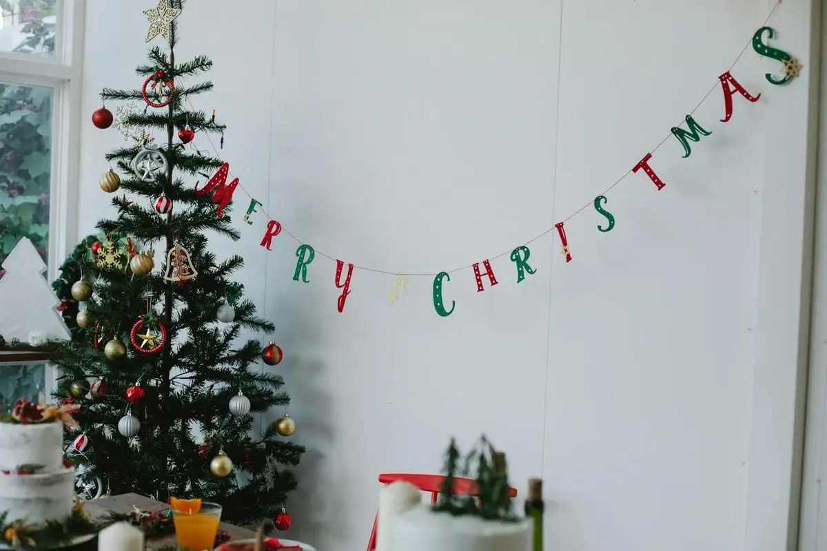 A beautifully decorated Christmas tree with a festive 'Merry Christmas' banner indoors.
