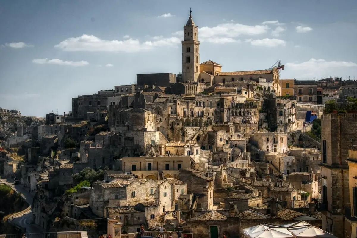 Aerial view of Matera, Italy's ancient stone cityscape under a blue sky.