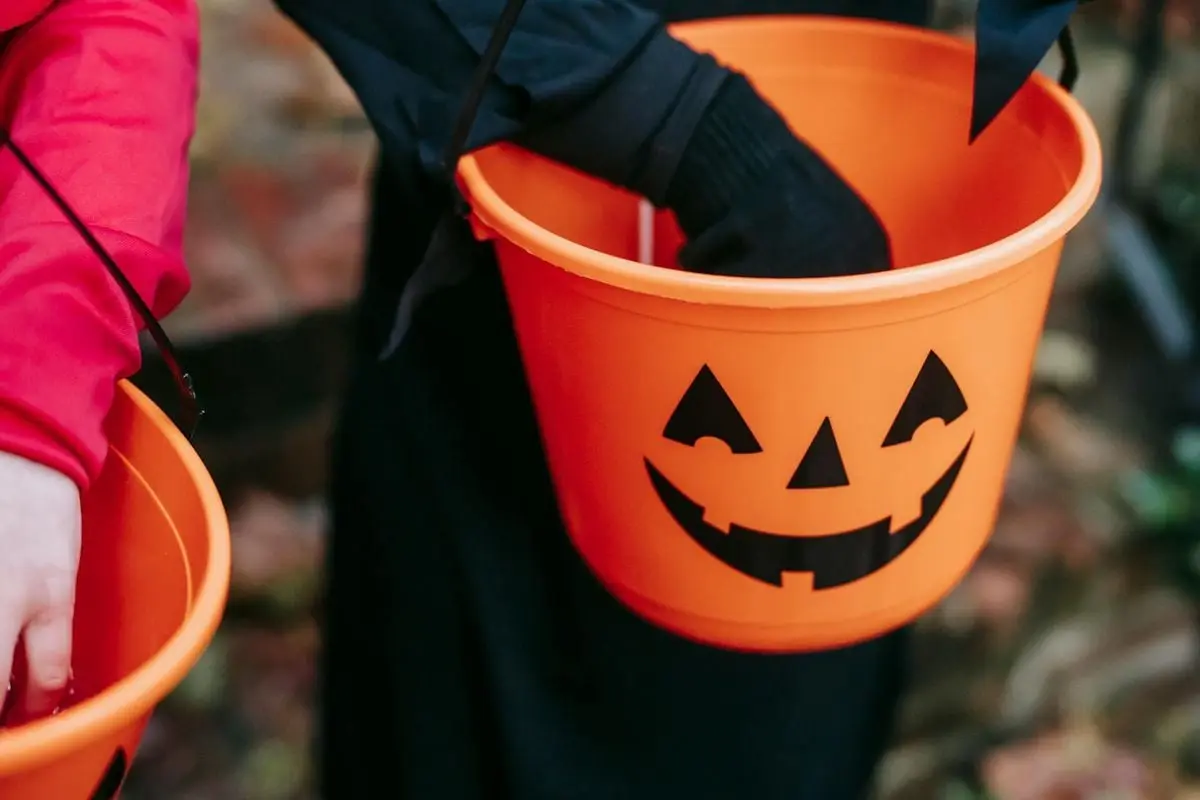 Children trick-or-treating with orange pumpkin buckets on a fall evening.