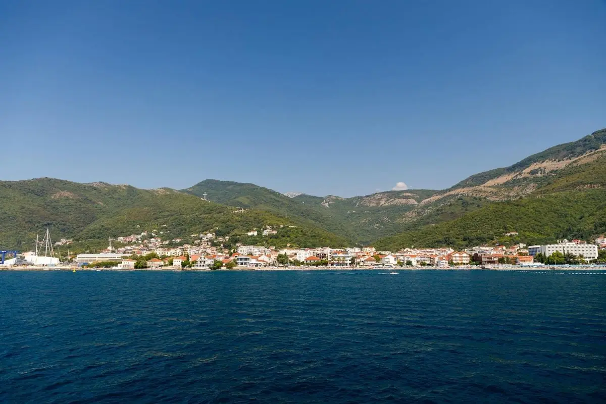 Charming coastal town nestled between lush mountains and vibrant blue sea under clear skies.