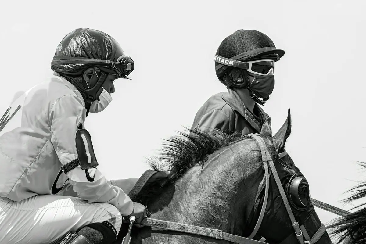 Two jockeys on horses, in black and white, during a race.