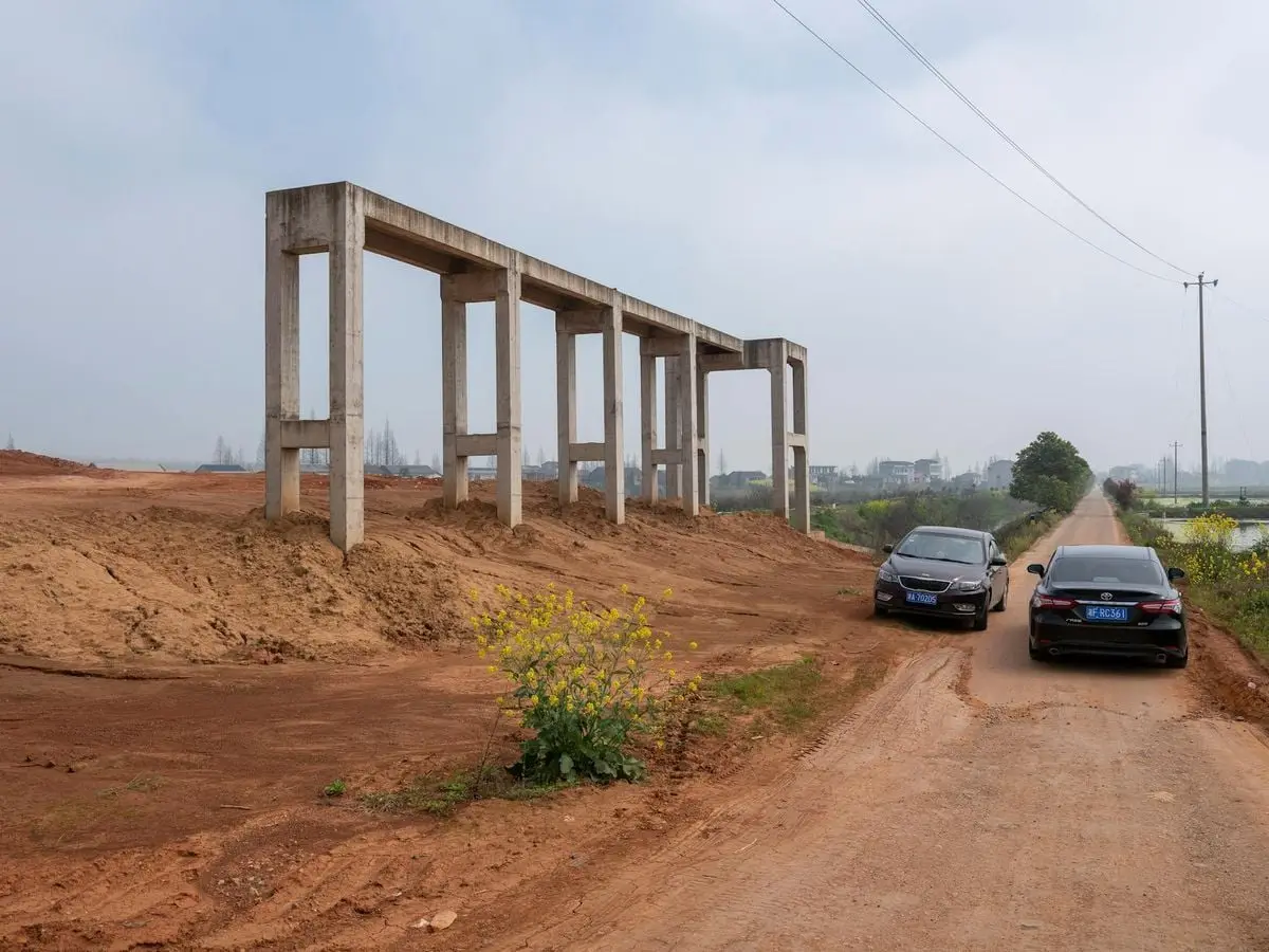 Rural scene with concrete beams, cars, and dirt road beside fields, capturing countryside development.
