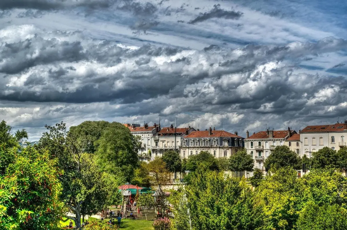 Scenic view of a charming French town with dramatic clouds and lush greenery.