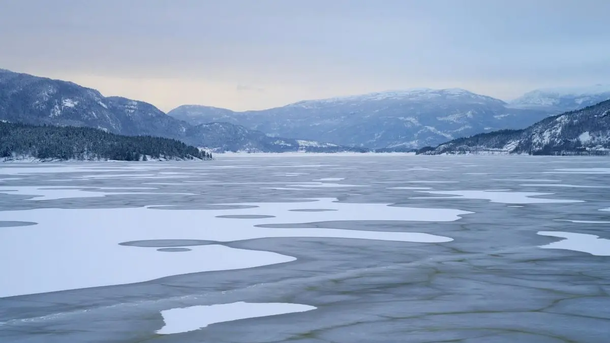 Panoramic view of a peaceful frozen lake surrounded by snow-covered mountains in winter.
