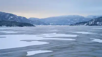 Panoramic view of a peaceful frozen lake surrounded by snow-covered mountains in winter.
