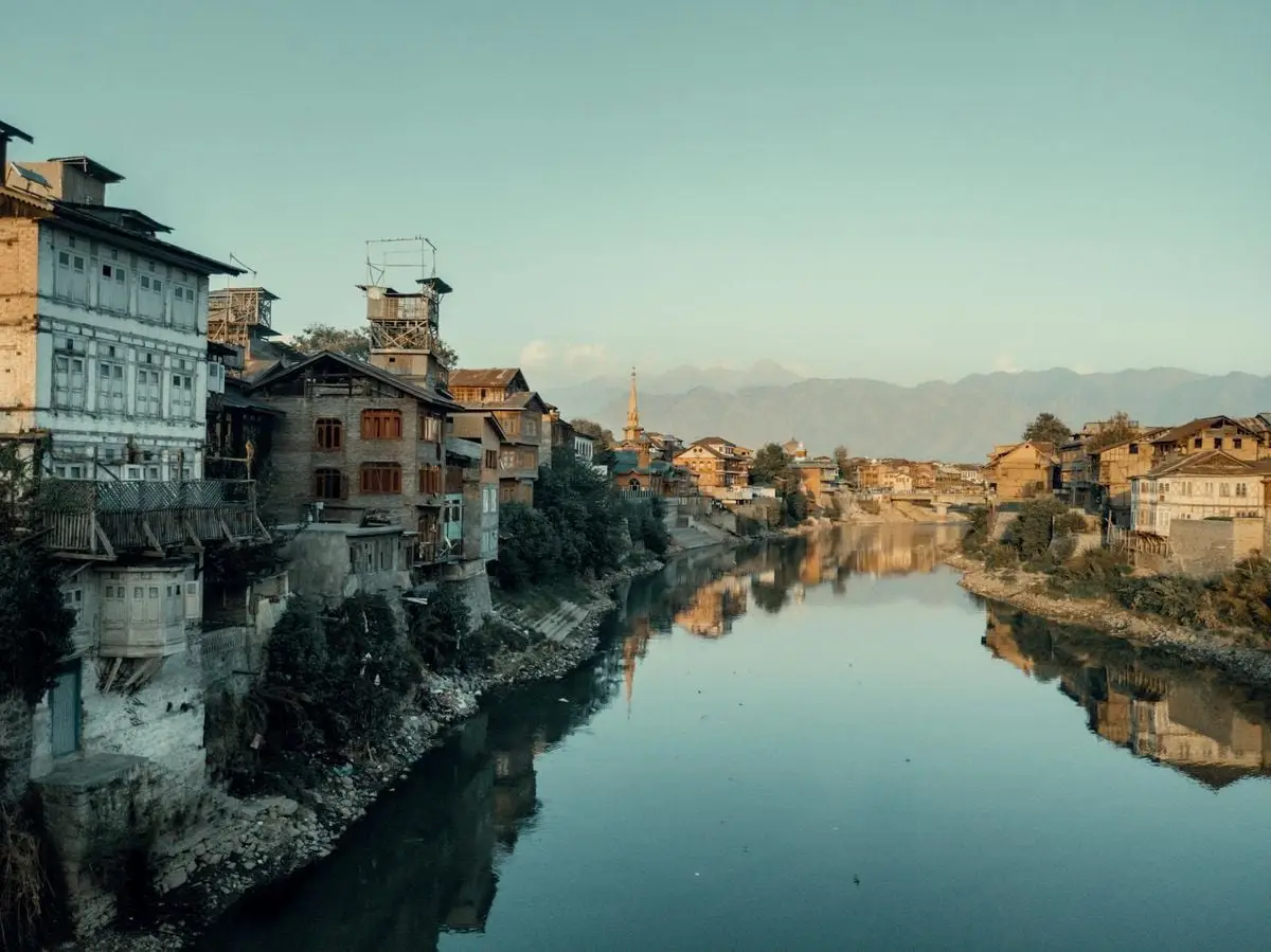 Scenic river dividing a rustic town with mountains in the backdrop, captured in soft evening light.