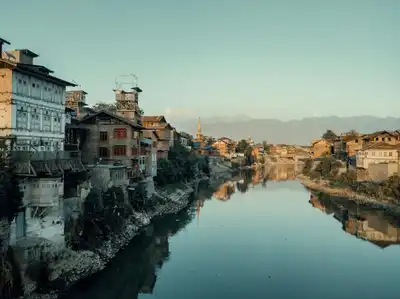 Scenic river dividing a rustic town with mountains in the backdrop, captured in soft evening light.