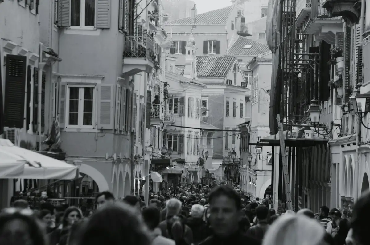 Black and white photo of a crowded street in Corfu, Greece. Captures lively urban atmosphere.