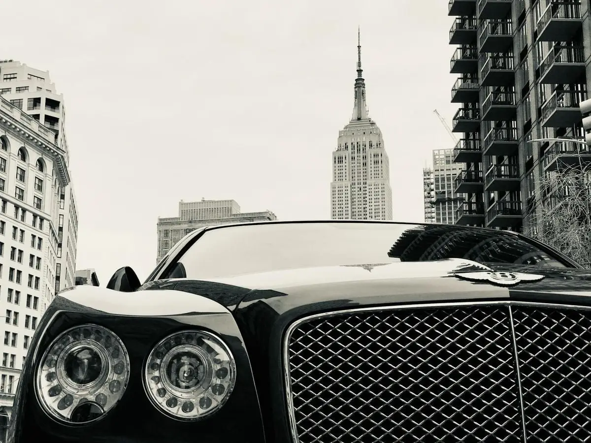 A striking black luxury car set against a bustling cityscape and iconic skyscraper.