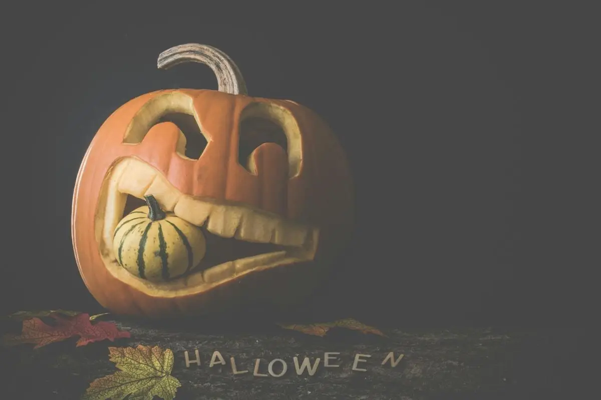 A carved pumpkin with a smaller gourd inside, surrounded by leaves and 'Halloween' letters.