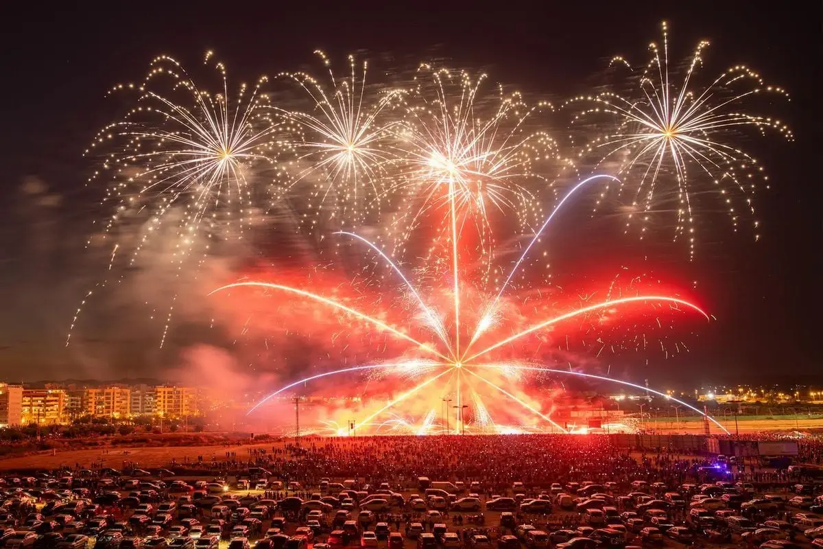 Spectacular fireworks illuminate the night sky over a bustling outdoor festival crowd.