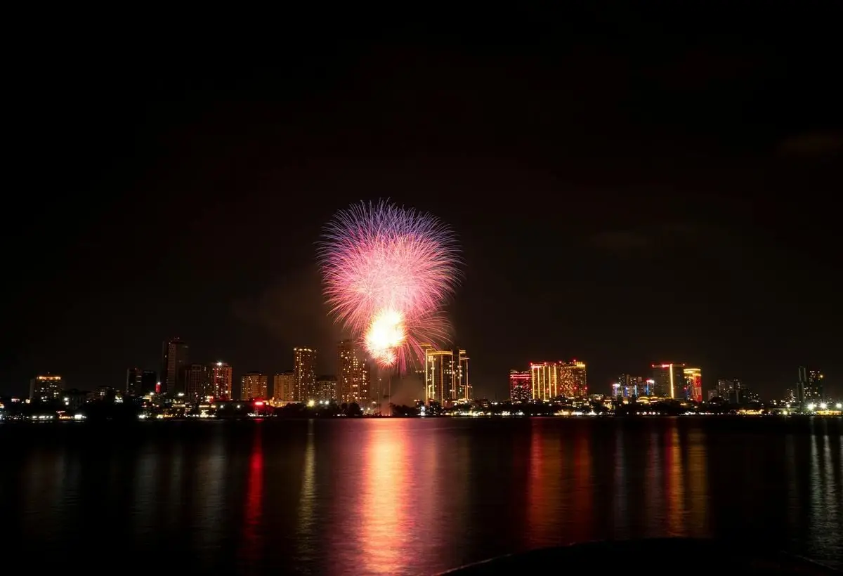Stunning fireworks display illuminates the night sky over a city skyline, reflecting vibrant colors on the water.