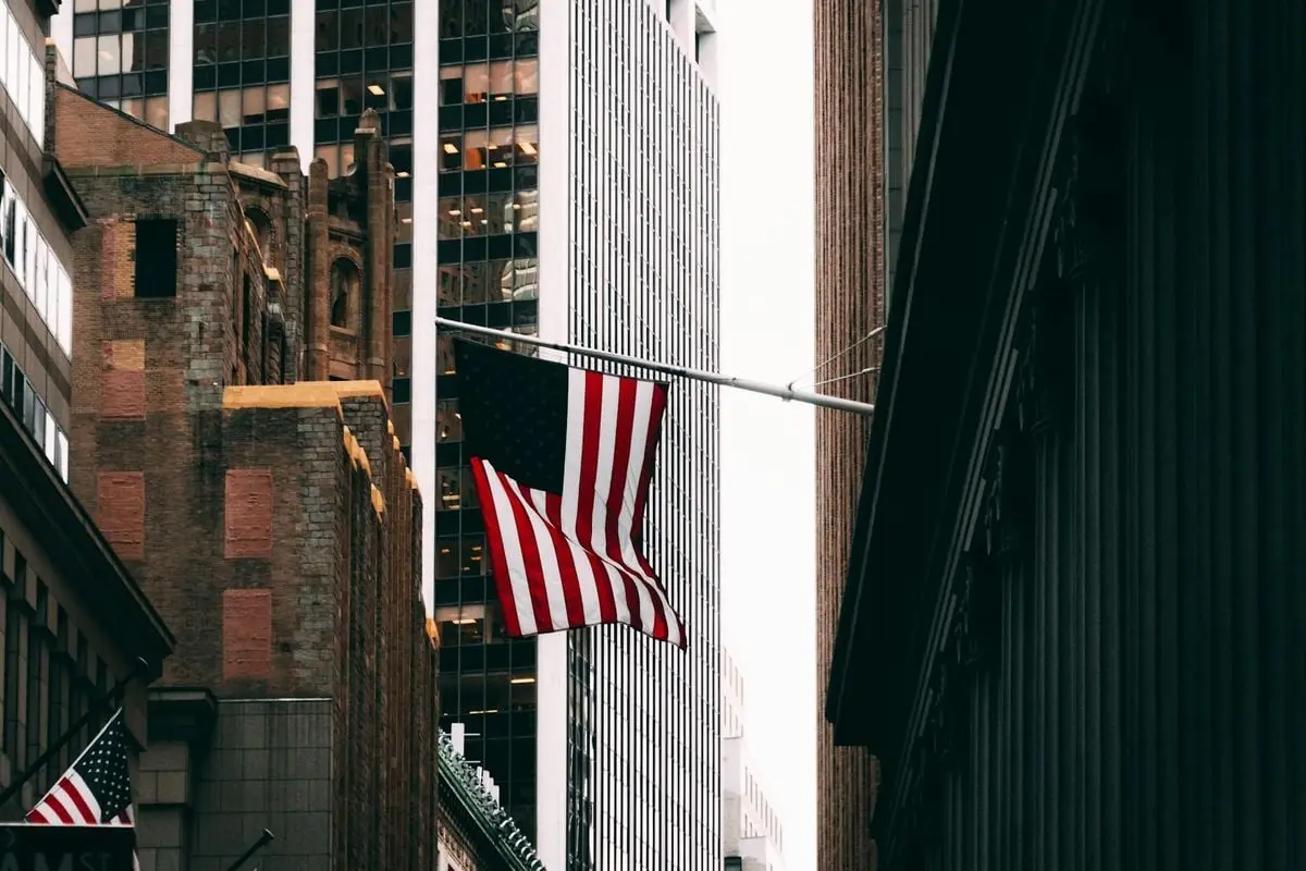Skyscrapers and American flag in a bustling city financial district street scene.