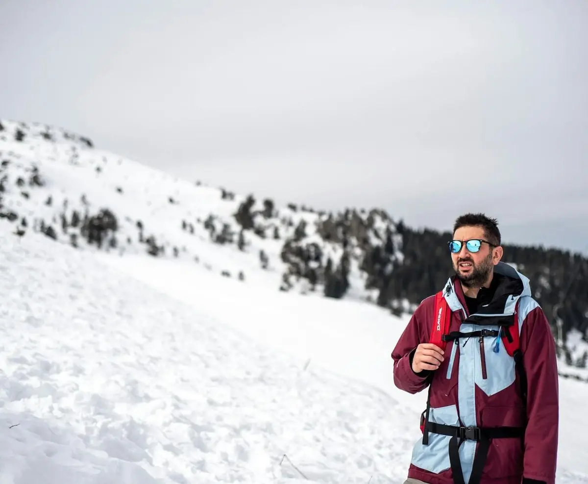 Man dressed in winter attire standing on a snowy mountain, reflecting a winter adventure setting.