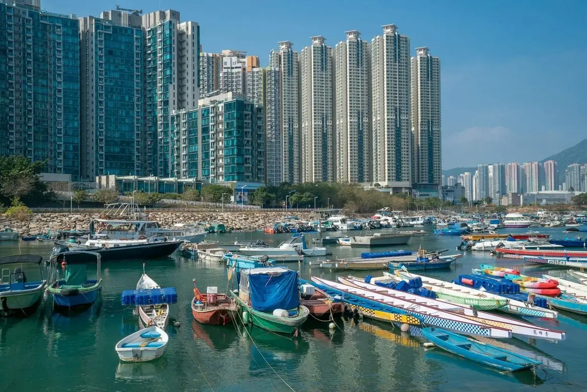 Skyscrapers and colorful boats along the bustling Hong Kong waterfront.