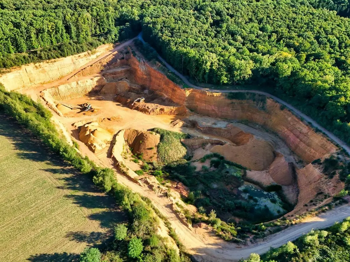 A stunning aerial shot of a large quarry contrasting sharply with lush green forests.