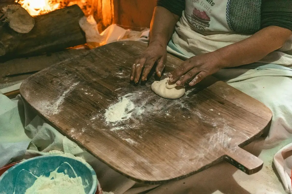 A person kneads dough by a cozy fireplace, capturing traditional Turkish bread making indoors.
