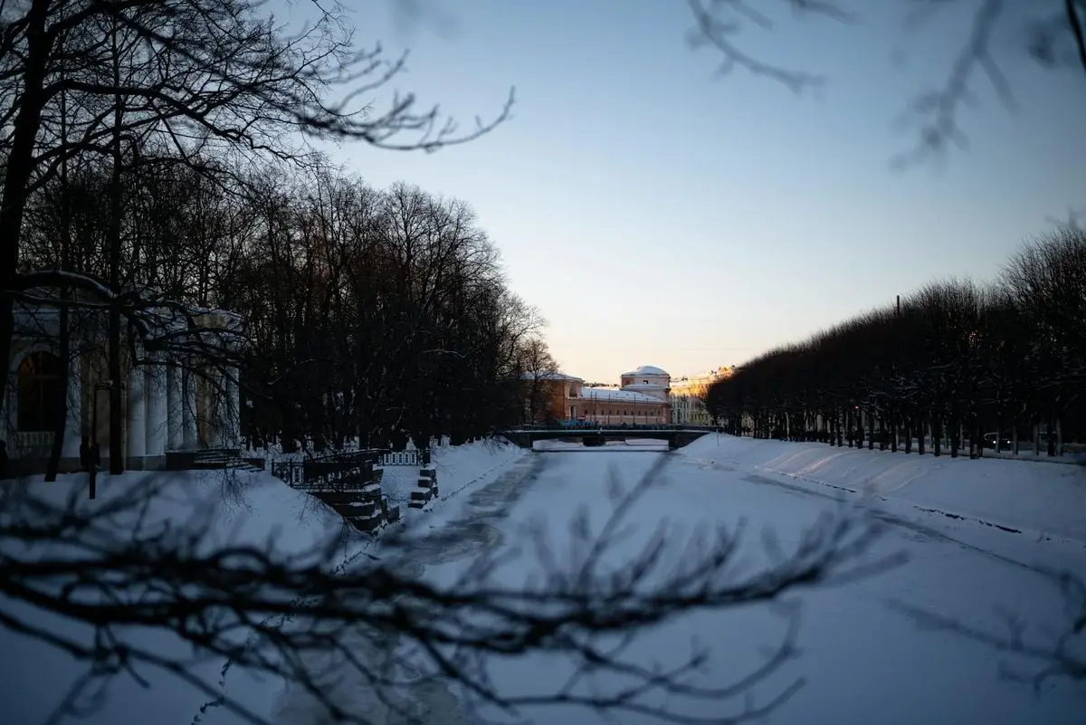 Scenic view of a snowy canal and bridge during winter sunset in Saint Petersburg, Russia.