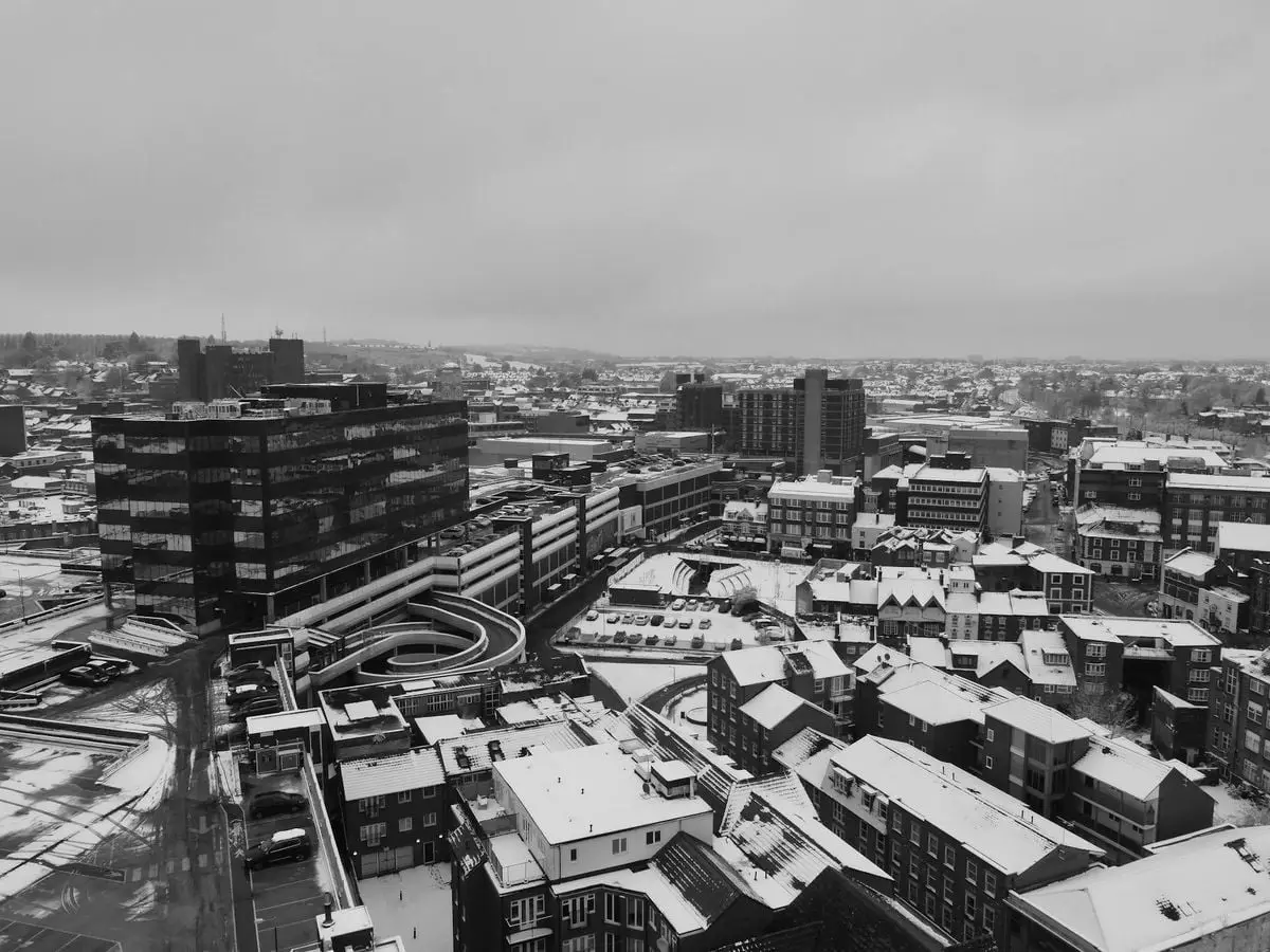 Black and white aerial view of snowy Luton cityscape during winter, showcasing buildings and roads.