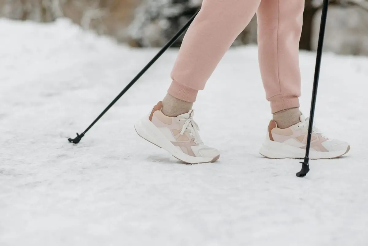 A person wearing sneakers and pink pants walking with poles on snow-covered ground in winter.
