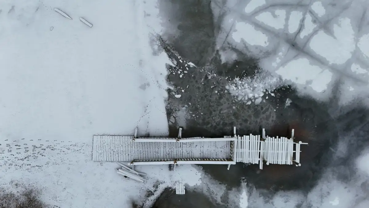 Aerial view of a snow-covered pier over a frozen lake in a tranquil winter setting.