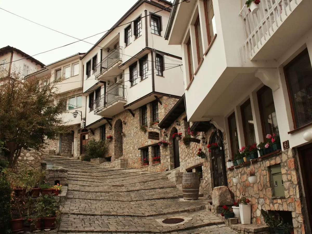 A cobblestone street in Ohrid, showcasing traditional Balkan Ottoman architecture with stone and white facades.