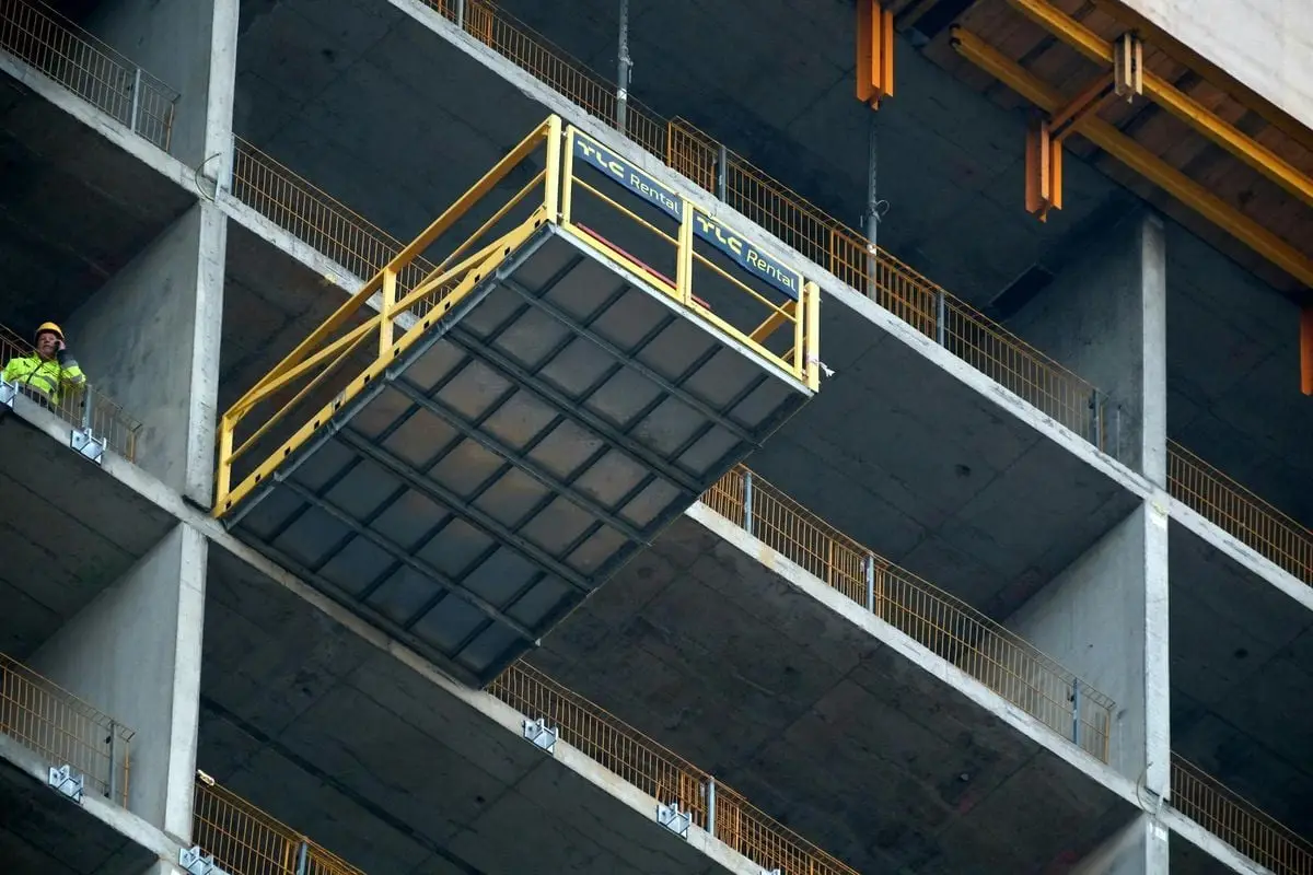 A construction worker supervises a platform lift at a high-rise building site.