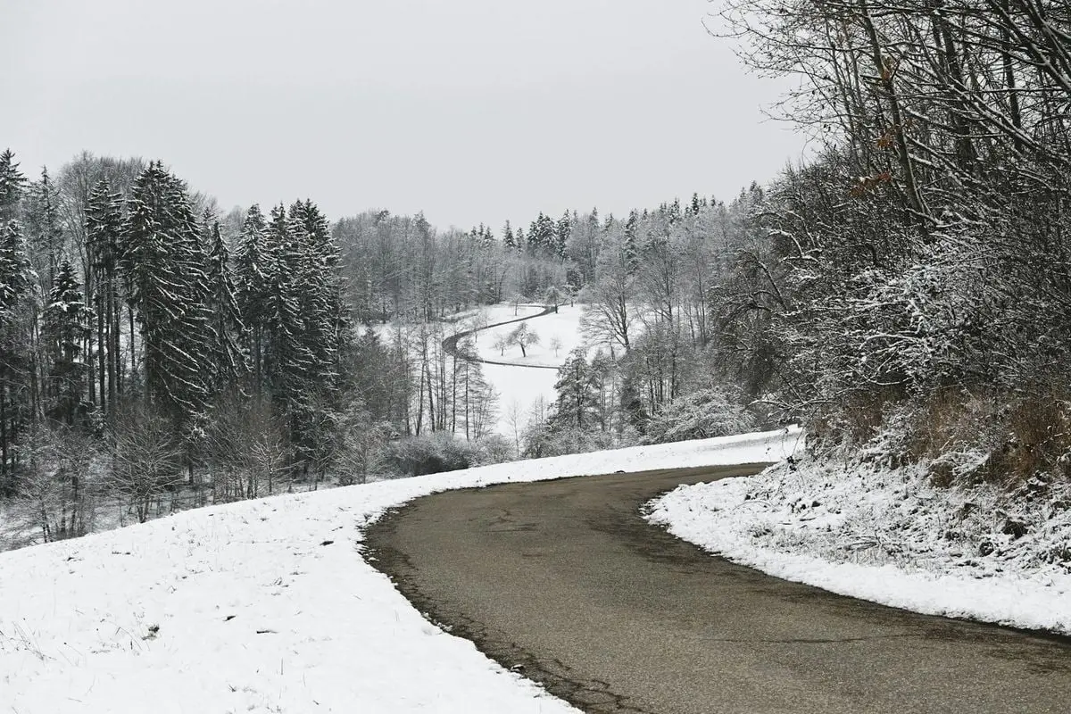 A snowy road winding through a winter forest in Auenwald, Germany.