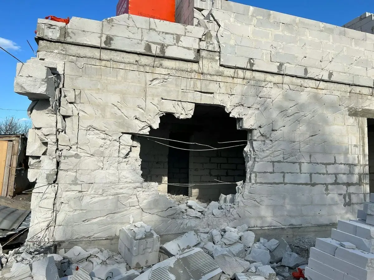 Concrete building wall with a large hole, showing damage and rubble, under a clear blue sky.