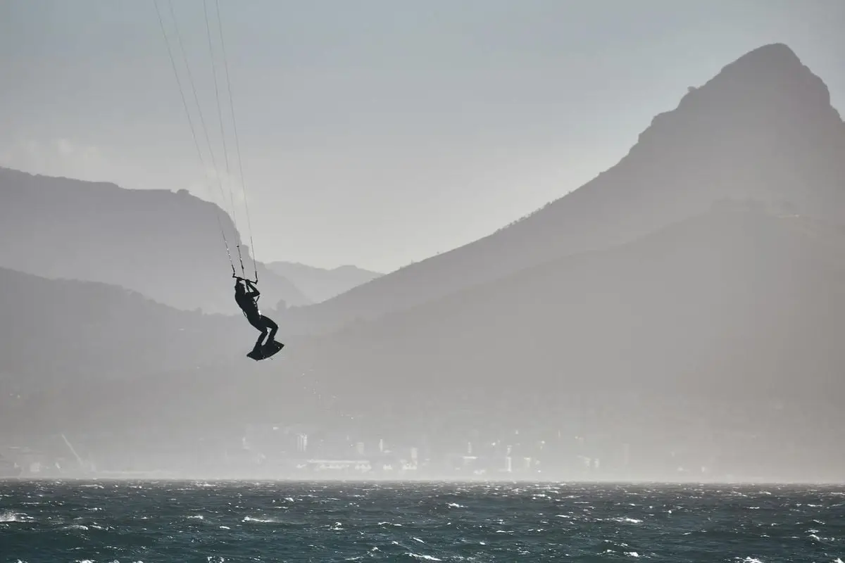 Silhouette of a kitesurfer jumping over ocean waves with Cape Town's iconic mountains in the background.