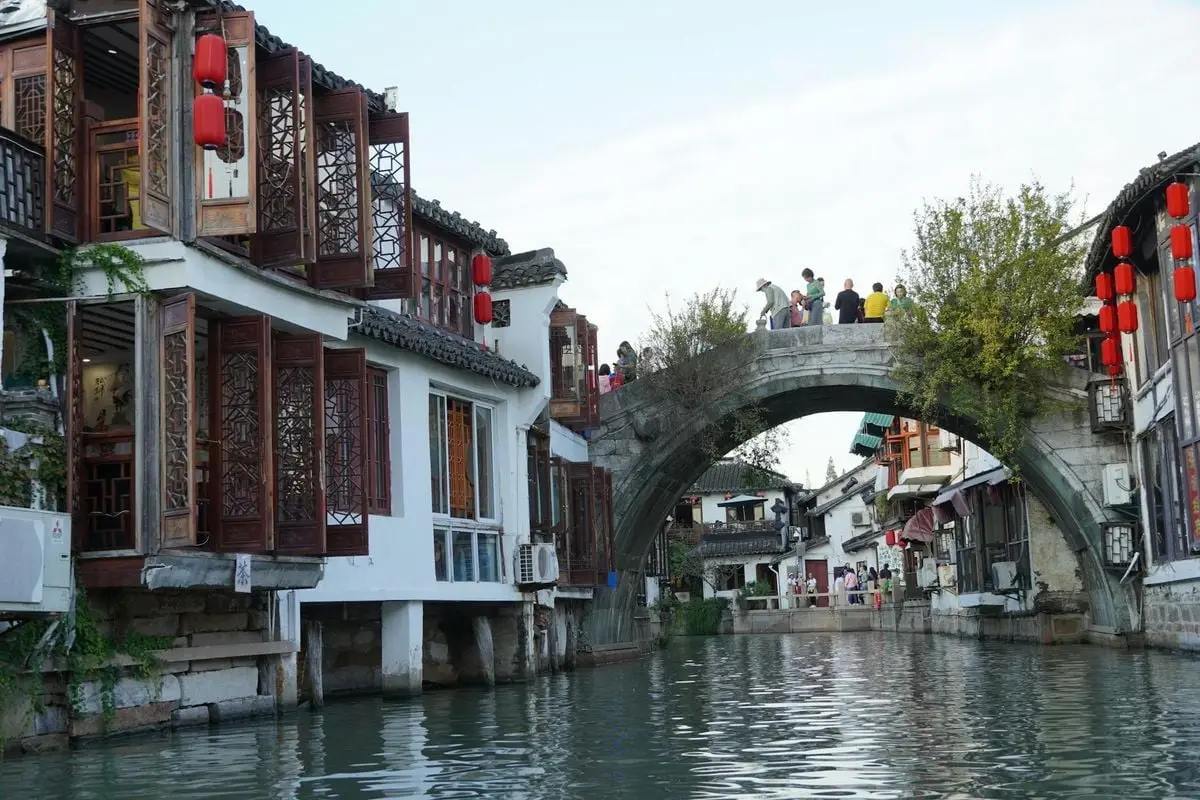 Scenic view of a traditional Chinese canal with buildings and an arch bridge adorned with red lanterns.