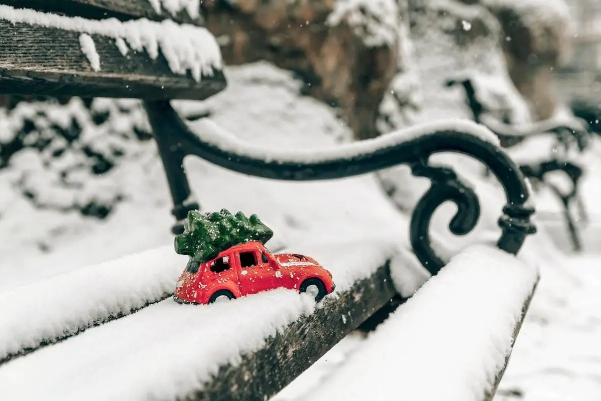 A miniature red car with a Christmas tree on a snowy bench captures the essence of a frosty winter holiday.