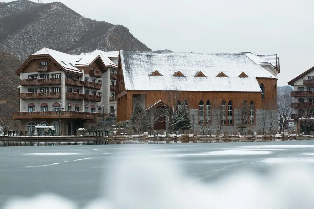 Snow-covered buildings by a frozen lake in a mountain town during winter.