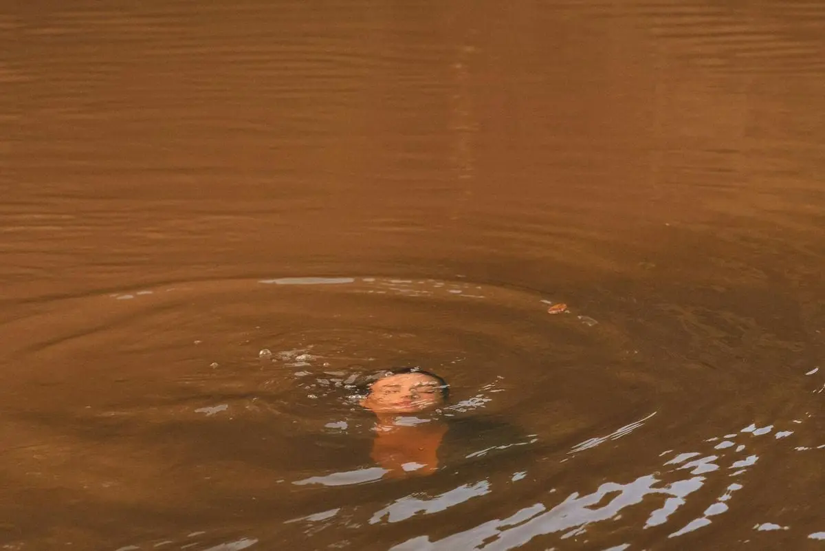 A person partially submerged in a warm-toned lake, creating ripples in calm water.