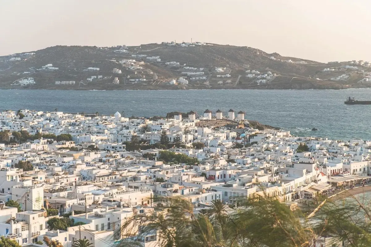 Captivating aerial view of Mykonos Town with iconic windmills and Aegean Sea backdrop during day.
