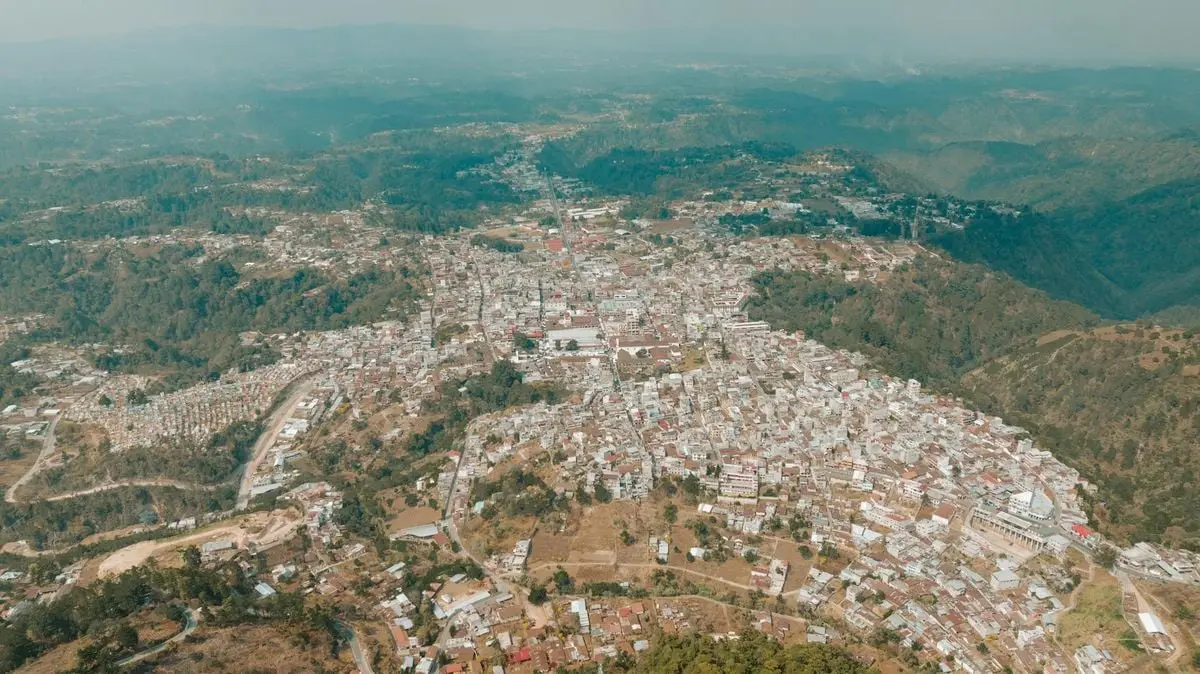 Drone shot of a scenic town nestled in green hills and mountains.