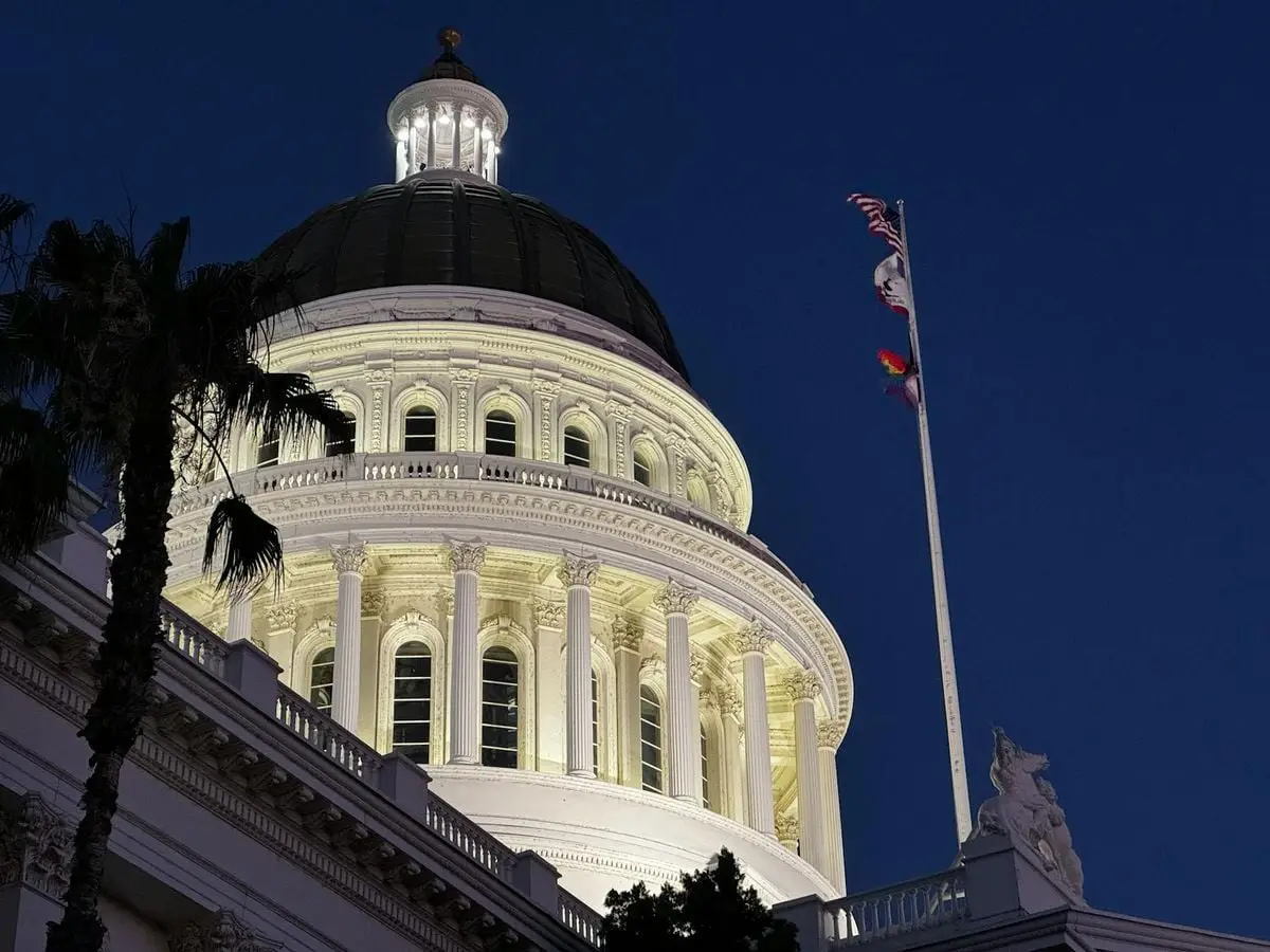 Illuminated California State Capitol dome with flags at dusk, Sacramento, USA.