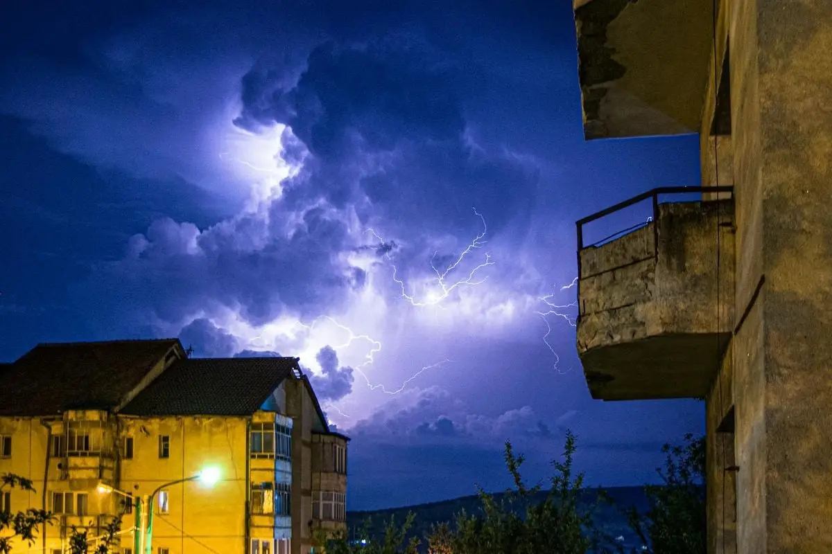 A vivid lightning strike during a nighttime thunderstorm, illuminating urban buildings.