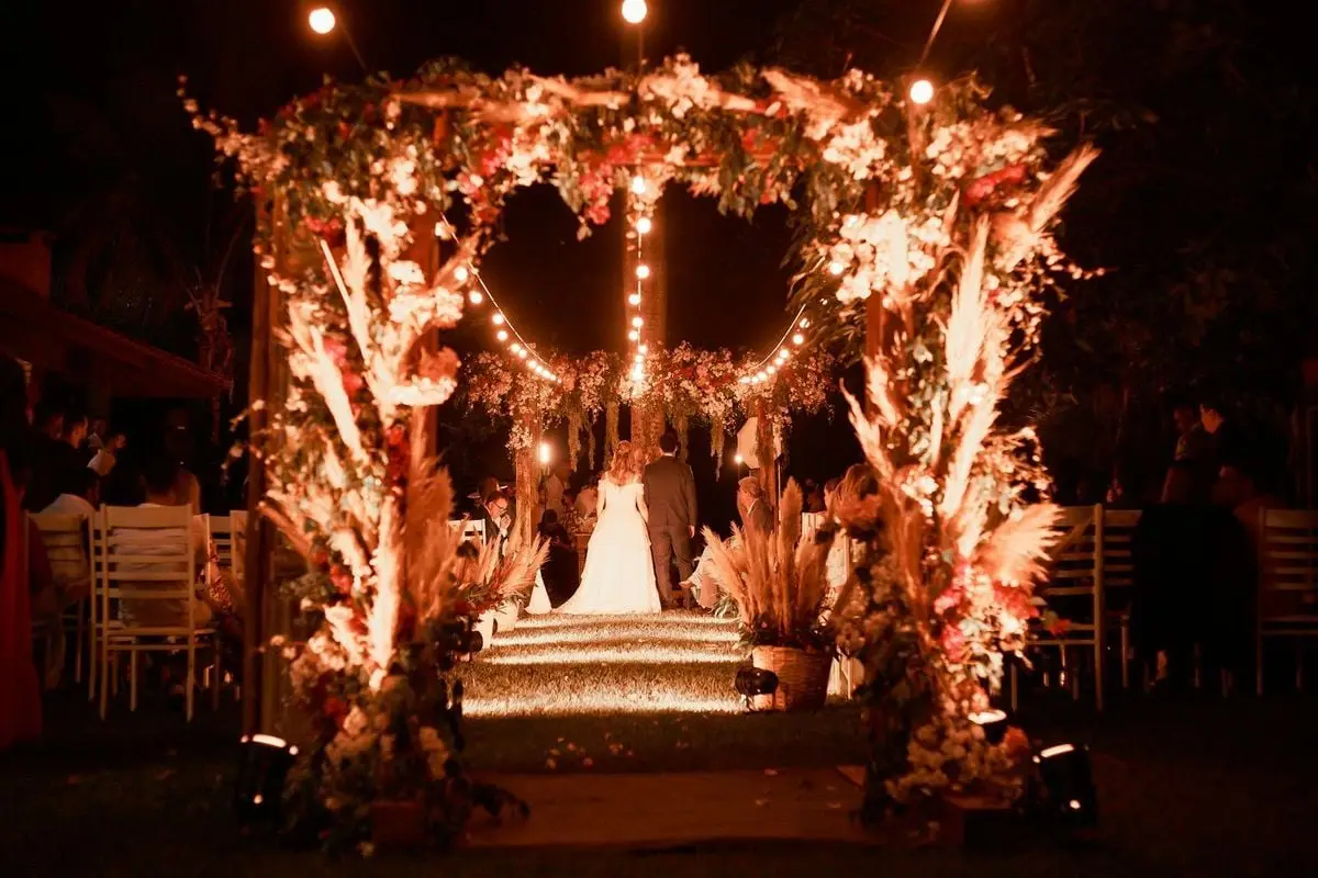 Enchanting wedding ceremony under illuminated floral arch at night.