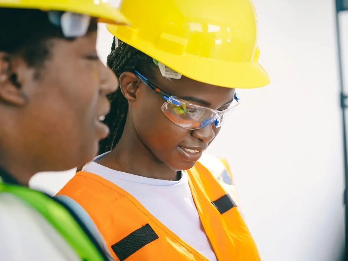 Two women engineers on site with hard hats and safety vests focusing on a task.